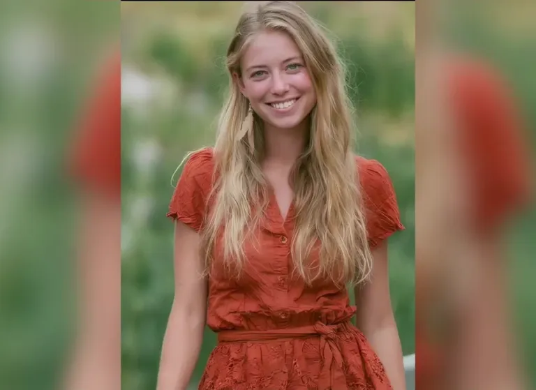 A blonde young woman in a rust-orange button-up dress stands smiling in a sunlit garden with soft green foliage behind her, a real-person input photo for an AI breast expansion video